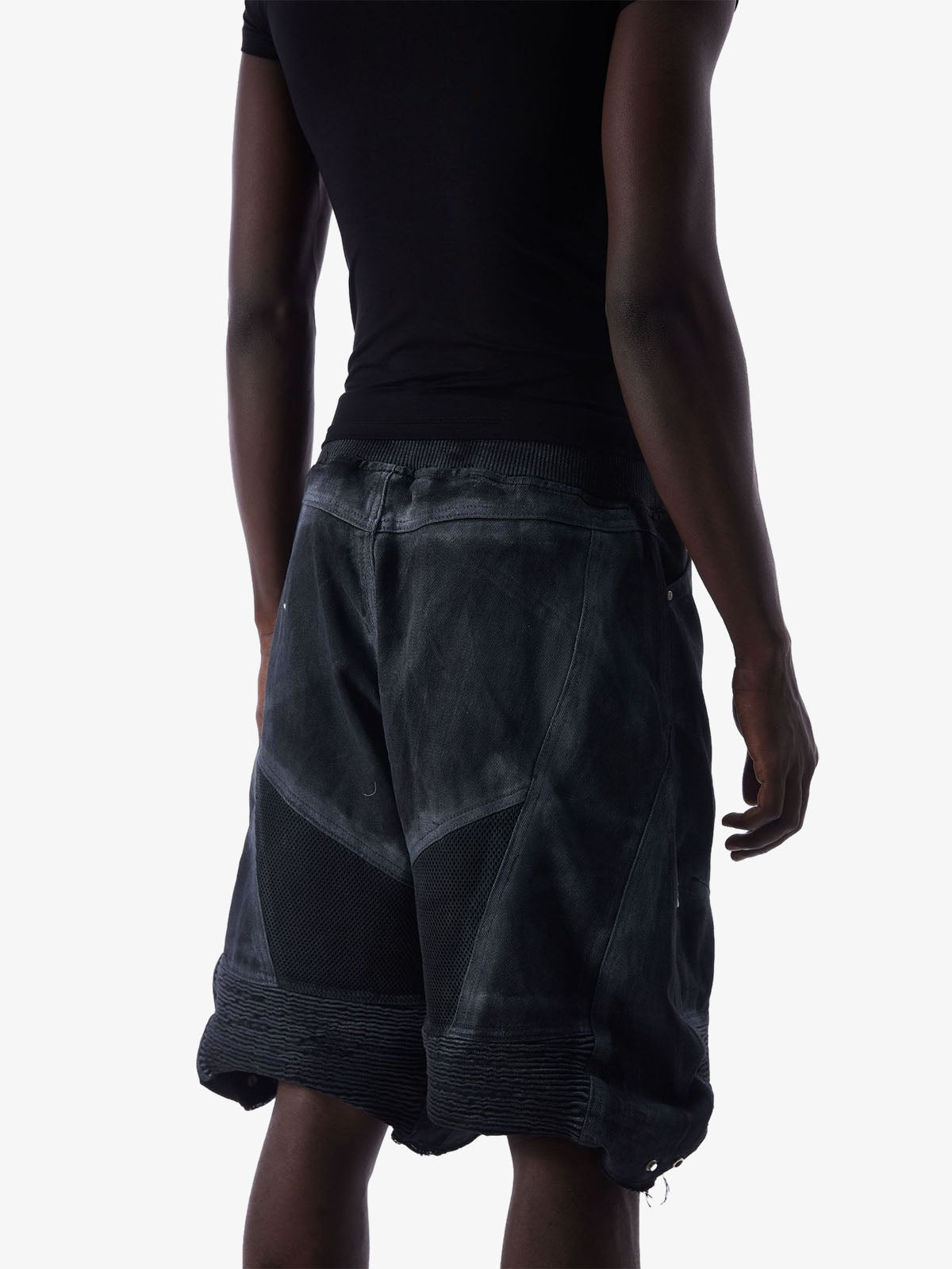 Angled back view of denim shorts with layered construction and mesh panels